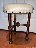 Full view of the antique metal stool showing upholstered seat and metal legs with decorative elements
