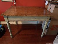 Front view of antique pine kitchen table showing rectangular wood top and green painted turned legs with crackle paint finish.