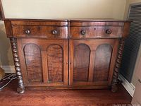 Front view showing two drawers with wooden knobs and two doors with book-matched veneer and carved spiral column legs on sides.