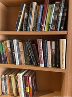 Three shelves of novels showing a mix of hardcover and paperback books by multiple authors, mostly fiction.