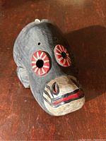 Front-left angle view of the black carved wooden mask with red and white painted eyes and animalistic mouth