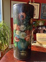 Full front view of the cylindrical wooden umbrella stand showing hand painted colorful floral bouquet in a blue vase on a dark background.