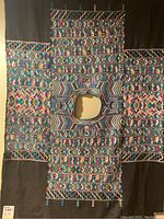 Full view of black hand woven Huipil with colorful geometric and diamond patterns and neck opening.