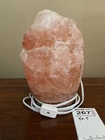 Front angled view of rough pink and white Himalayan salt lamp on base with electric cord and inline switch coiled at base.