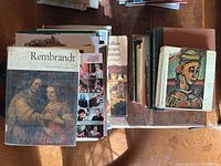 Top-down view of a large collection of art books spread in two stacks displaying titles such as Rembrandt, Linda Rogers, Italian landscape artists.