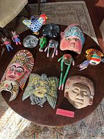 Large Mexican decor lot displayed on a round wooden table including several colorful masks, animals figurines, and sculptures.