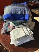 Stack of various vintage table linens, runners, lace pieces, and napkins in different colors and textures on a wooden table under sunlight