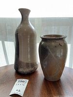 Tall and shorter mid century pottery vases placed on wooden surface with light behind showing glaze finish and shape details