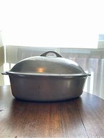 Front view of large metal roasting pan with lid on wooden surface near window light.
