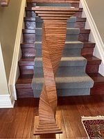 Front view of the wood spiral pedestal standing on a wood floor with stairs in background.