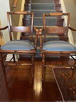 Front view of the pair of antique wooden chairs showing the blue satin seats and wood details.