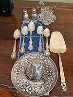 Overview of all lot contents: teaspoons on blue pouch, salt & pepper shakers, pie server, ashtray on tray, glass pick holder with metal picks