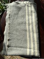 Folded vintage grey wool blanket with white stripes displayed on a surface, showing the overall color and pattern.