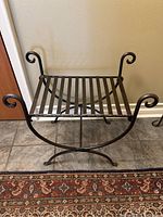 Front view of wrought iron bench showing slatted seat, scrolled ends, and curved X-frame legs