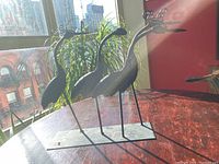 Side view showing the four metal wrought iron birds on base with one bird’s missing feathers visible on the head.