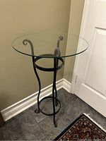 Photo showing the side view of the wrought iron table with circular glass top, highlighting curved legs and frame design.