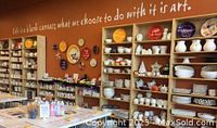 Photo of the interior pottery painting studio with shelves filled with white and colorful pottery pieces and supplies.