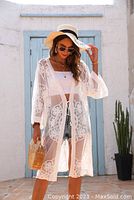 Photo showing woman wearing a sheer white lace coverup over a white crop top and shorts with a sun hat and sunglasses, representing the style of women's clothing available at Sweet Pea Boutique.