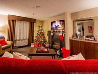 Living area with Christmas tree, red sofa, coffee table, fireplace and wall-mounted TV.