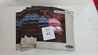 Photo showing a stack of seven 1983 Ford Mustang brochures with a red Mustang and man on the cover, labeled with the lot number.