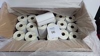 Box top view showing 36 white thermal label rolls inside a cardboard box with one roll placed on top.