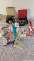 Lot of assorted fishing gear including Daiwa CX135 fishing reel in box, lures, hooks and other accessories spread on surface