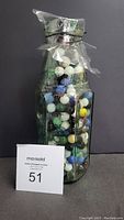 Front view of old glass bottle filled with assorted colorful marbles, sealed with plastic wrap and tied with string.