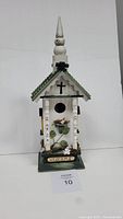 Front view of rustic wooden bird house showing green roof, cross design and welcome sign on base