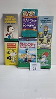 Front view of 6 Peanuts VHS tapes lined up showing titles and cover art with Snoopy and Charlie Brown characters, 2 tapes unopened.
