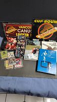 Wide shot showing all items in the lot including the Vancouver Canucks sign, Olympic books, and multiple sports/hockey cards.