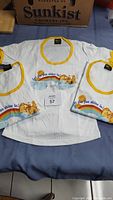 Three vintage white youth large Care Bears T-shirts with yellow trim, laid flat showing front graphics with rainbow and sun