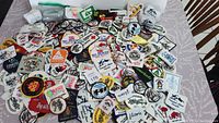 Overhead view of a large pile of vintage patches and crests displayed on a tabletop showing varied shapes, colors, and designs including logos, text, and mascots.