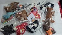 Full lot of 12 vintage Ty Beanie Babies in plastic bags, assorted animals and designs laid out on white surface