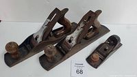 Front view of two large and one small Stanley wood planes with wooden knobs and handles, showing rusty metal parts and used condition.