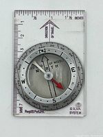 Clear rectangular base compass with metal dial, cardinal directions, and measurement markings.