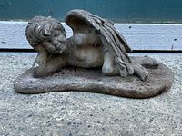Side view of the concrete garden angel statue reclining with wings extended along its back.