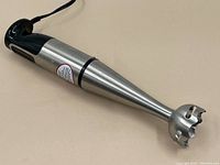 Cuisinart hand blender lying on a light surface, showing stainless steel blending arm and black handle with power cord.