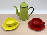 Photo showing the full tea pot and two teacup sets with saucers, yellow and red.