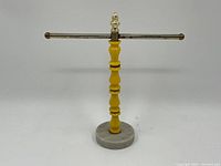 Full view of the vintage face cloth stand with yellow wooden post, metal horizontal bar with ball finials, and marble base.