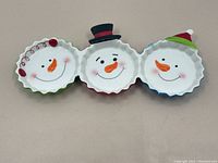 Front view of the triple connected ceramic dish showing three smiling snowmen with different hats and scarves.
