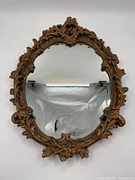 Front view of oval mirror with ornate gold floral frame showing carved details and aged finish.