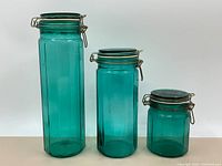 Full view of three vintage blue-green glass resealable jars of varying heights, with metal clamp locking lids