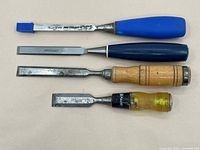 Top view of four wood chisels showing handles and blades with one blue blade cap attached to one chisel.