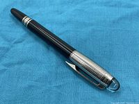 Full pen view on blue background showing black grid-patterned barrel and chrome cap