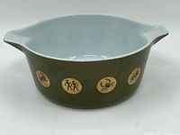 Front side view of the Pyrex casserole dish showing olive green body with zodiac symbols around.
