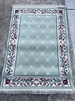 Full view of the rectangular Sears brand rug showing light green center with white diamond lattice and floral cream border with fringe tassels on ends.