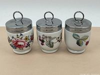 Front view of 3 porcelain jars showing floral patterns and metal lids with loop handles