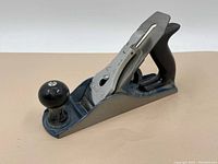 Side angle view of the Stanley hand planer showing dark blue metal body, front knob, rear handle, and metal blade lever cap.