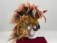Front view of vintage Whimsey Wear feather mask on white mannequin head showing colorful feathers and faux leaves covering the face.