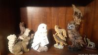 Photo showing multiple animal figurines on a wooden shelf including owls, raccoon, squirrel, rabbit, fox, and others.